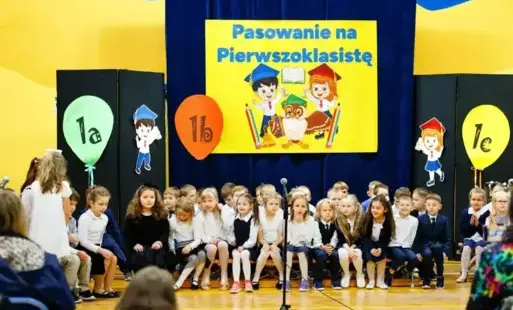 Pierwszoklasiści siedzący na ławkach w trakcie uroczystości pasowania